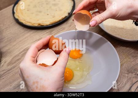Woman's hands cracking eggs into a bowl, preparing for breading or cooking Stock Photo