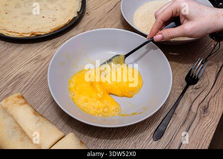 Woman preparing ingredients, beating raw eggs in a bowl with a spoon Stock Photo