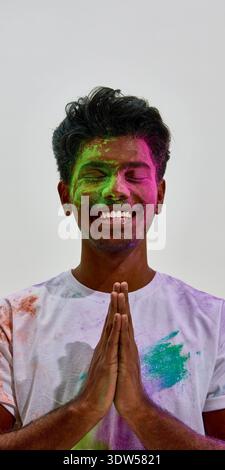 Smiling man with hands in namaste covered in colored powder. Stock Photo