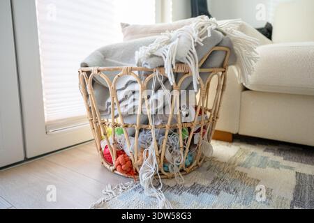 Woven rattan basket with cozy blankets and yarn in Scandinavian home interior Stock Photo