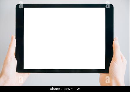 Close-up of hands holding a modern tablet with blank white screen, isolated on light background. Ideal mockup for app presentation, responsive design, Stock Photo