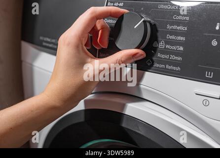 Hand selecting washing program on machine panel. Fingers turning control knob choosing cycle. Household appliance operation concept. Stock Photo