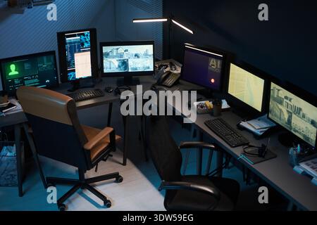Empty office workspace featuring multiple computer monitors displaying surveillance footage and data analysis, ergonomic chairs positioned around desks, modern technology setup Stock Photo