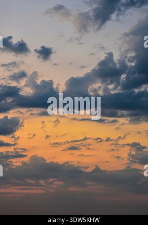 A tall vertical shot of the evening sky showing layers of dark clouds over a bright orange horizon light. Stock Photo