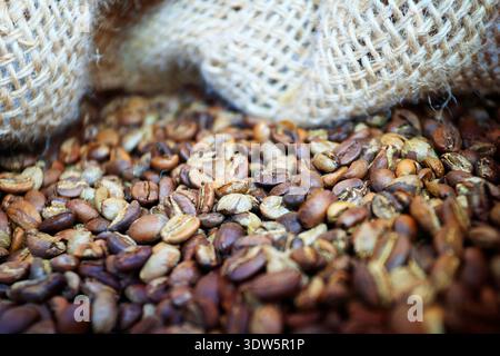 Roasted coffee beans spilling out of burlap sack, close-up macro photography Stock Photo