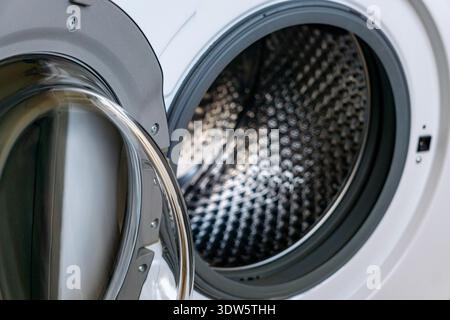 Side view of an open front loading washing machine showing detailed stainless steel drum texture. Stock Photo