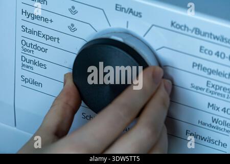 Close up of a person adjusting the washing machine program using the control knob. Focus on the modern appliance interface and laundry settings panel. Stock Photo