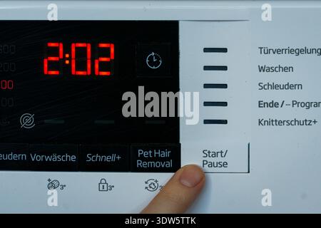 Close up of a finger pressing the start button on a modern washing machine digital panel. Stock Photo
