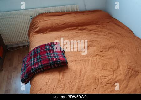 Christmas plaid folded on the side of bed with orange linen. Everyday home scene with seasonal textile and warm color contrast. Stock Photo
