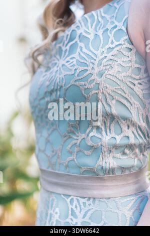 A woman is wearing a blue dress with silver flowers on it. The dress is made of lace and has a silver belt. The woman's hair is styled in loose waves Stock Photo