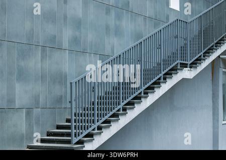 An external staircase ascends alongside a building featuring a contemporary, vertically paneled gray wall, offering a sense of upward movement and arc Stock Photo