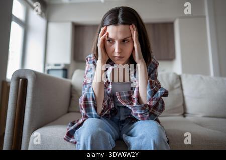 Thoughtful distressed woman sitting alone feeling stuck, mentally drained hands pressed to temples. Stock Photo