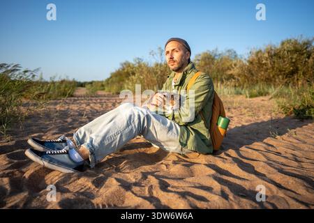 Thoughtful relaxed man rest on sandy beach holding cat in hands while enjoy fresh breeze together  Stock Photo