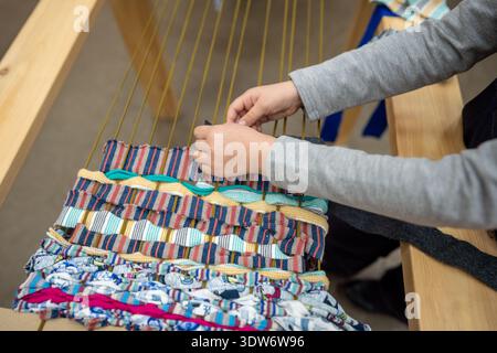 Weaving . Closeup child hands carefully weaves threads on loom in study traditional craft workshop. Stock Photo