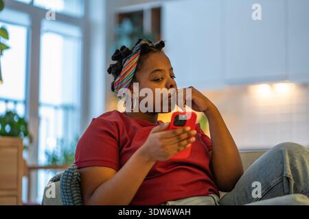 Upset woman feeling worried checking notifications, message on phone, social media overload at home. Stock Photo