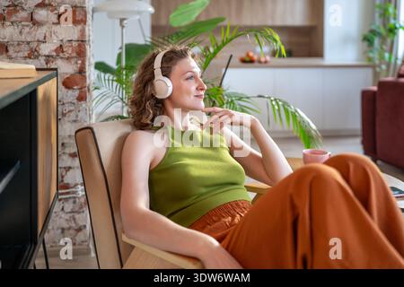 Thoughtful positive woman enjoying favorite playlist reflecting dreaming comfortable resting at home Stock Photo