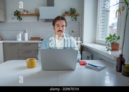 Thoughtful focused man using laptop remote work from home. Morning coffee, freelance internet job. Stock Photo