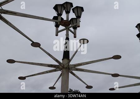 Vintage multi-arm street lamp with geometric metal structure against cloudy sky, urban lighting design and architectural detail. Stock Photo