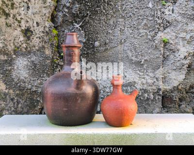 Two large and small clay jugs with a textured wall background Stock Photo