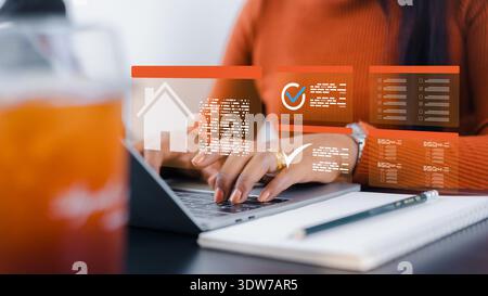 Woman using laptop with home icon and digital checklist interface. Concept of real estate online search, property investment, home loan application, a Stock Photo