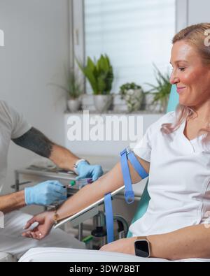 A healthcare worker performs a blood draw on a patient in a clinic to collect a blood sample for testing and analysis. Stock Photo