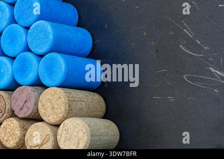 Close-up view of synthetic blue wine corks stacked above natural cork stoppers on a dark textured background. Stock Photo