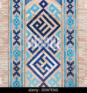 Ornate blue and turquoise tile mosaic panel with repeating Islamic geometric pattern set into a warm brick wall, offering decorative texture, cultural Stock Photo