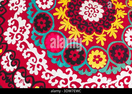 Bright traditional Suzani embroidery featuring circular floral medallions and swirling white motifs on red fabric background, evoking folk craftsmansh Stock Photo