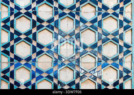 Ornate blue geometric Islamic tile pattern featuring repeating hexagon motifs and star shapes on an aged mosaic wall panel, highlighting traditional c Stock Photo