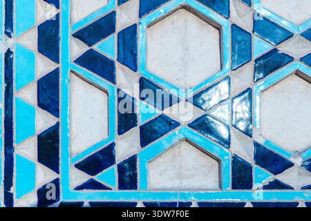 Close up of blue geometric Islamic tile pattern featuring repeating hexagon motifs and star shapes on an aged mosaic wall panel, highlighting traditio Stock Photo