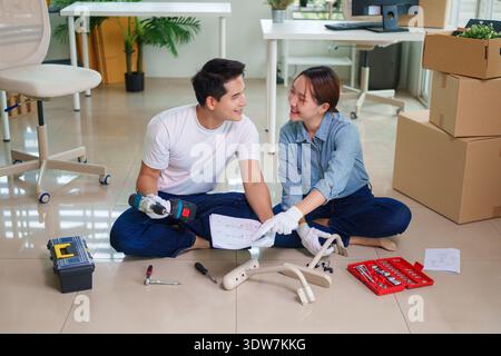 Asian adult couple collaborating assembling furniture with power tools DIY project for new apartment or office setup teamwork productivity Stock Photo