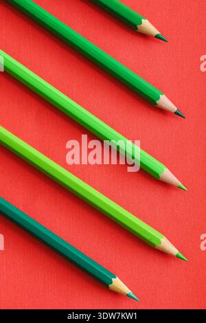 green colored pencils arranged diagonally on a vivid red background, illustrating complementary color contrast and dynamic minimal design. Stock Photo