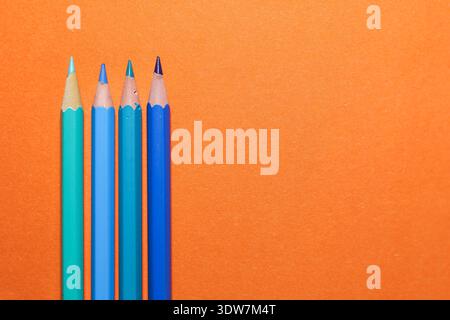 blue and orange pencils arranged in dynamic diagonal lines over a bold orange surface, illustrating complementary colour contrast Stock Photo