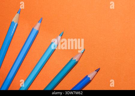 blue and orange pencils arranged in dynamic diagonal lines over a bold orange surface, illustrating complementary colour contrast Stock Photo