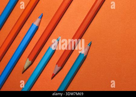 blue and orange pencils arranged in dynamic diagonal lines over a bold orange surface, illustrating complementary colour contrast Stock Photo