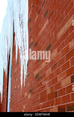 A row of long icicles hanging parallel to a red brick exterior wall on a cold winter day. Stock Photo