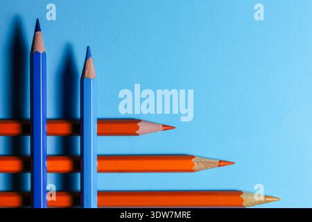 blue and orange pencils arranged in dynamic diagonal lines over a bold blue background, illustrating complementary colour contrast Stock Photo