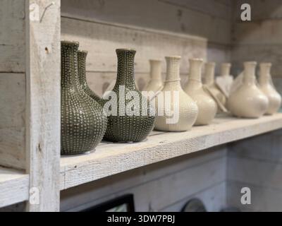 Row of neutral aesthetic, textured ceramic vases, on a rustic wooden shelf in an upmarket home decor and interiors store. Stock Photo