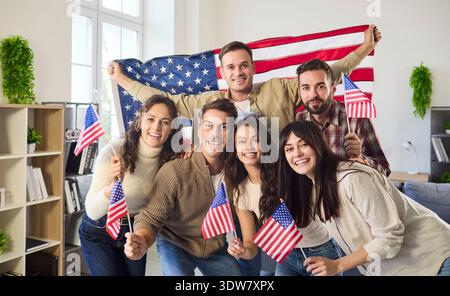 Friends celebrate US Independence Day indoors, smiling and waving American flags Stock Photo