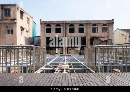 View of an old concrete factory building seen from a modern wooden viewing deck with metal railings, illustrating urban renewal. Stock Photo