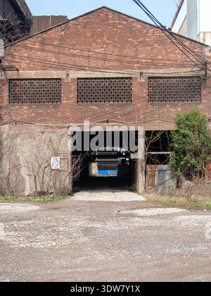 Front view of a vintage red brick warehouse building with a large open entrance leading into darkness, highlighting industrial heritage. Stock Photo
