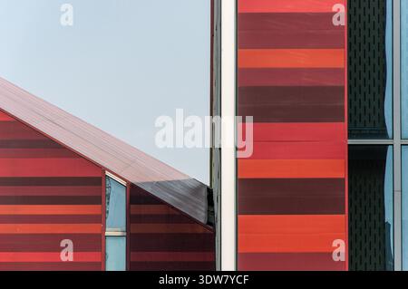Close-up abstract shot of a modern building's exterior wall featuring bold horizontal stripes in shades of red and brown, contrasting with glass eleme Stock Photo