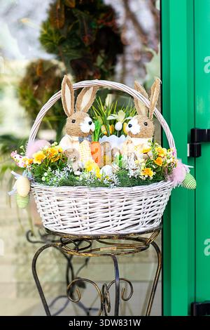 Easter basket with two plush bunny toys, flowers and decorative eggs on a metal stand Stock Photo