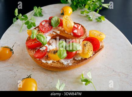 Round bruschetta with red and yellow cherry tomatoes and goat cheese on marble board. Farm produce, crusty bread. Food and healthy eating. Stock Photo