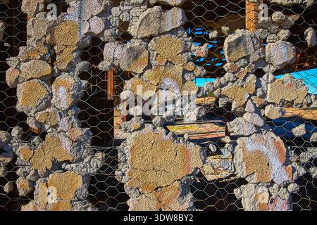 Textured Abandoned Wall With Wire Mesh And Exposed Structure In Harsh Desert Sunlight Stock Photo