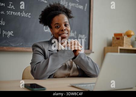 Portrait of Young Adult Black Woman Smiling While Sitting at Desk in Classroom Stock Photo
