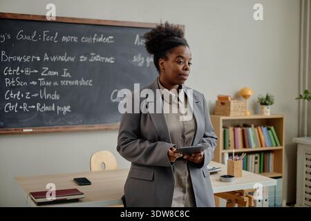 Young Adult Black Woman Teaching Lesson Using Digital Tablet in Classroom Stock Photo