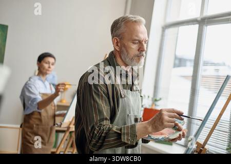 Middle Aged Caucasian Man Painting on Canvas Learning in Group Art Class  Stock Photo