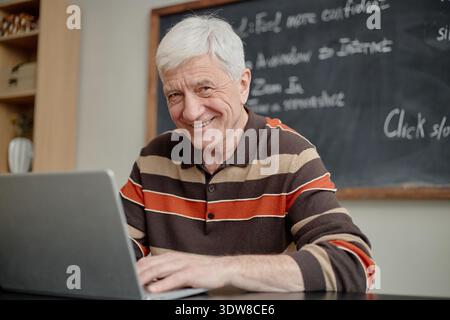 Senior Caucasian Man Smiling While Using Laptop during Educational Activity Stock Photo