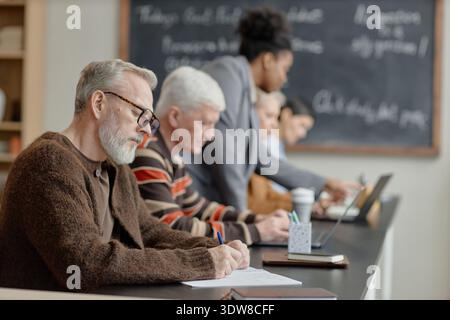 Middle Aged Caucasian Men Writing while Studying with Diverse Group in Classroom Stock Photo